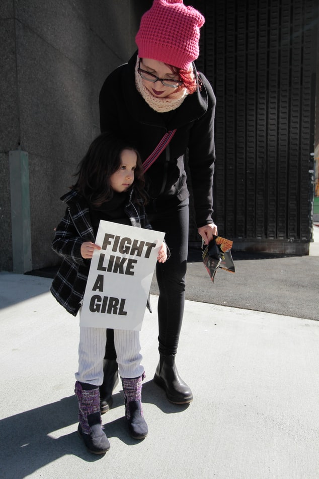 mum behind girl who is holding a sign that says fight like a girl mum behind girl who is holding a sign that says fight like a girl